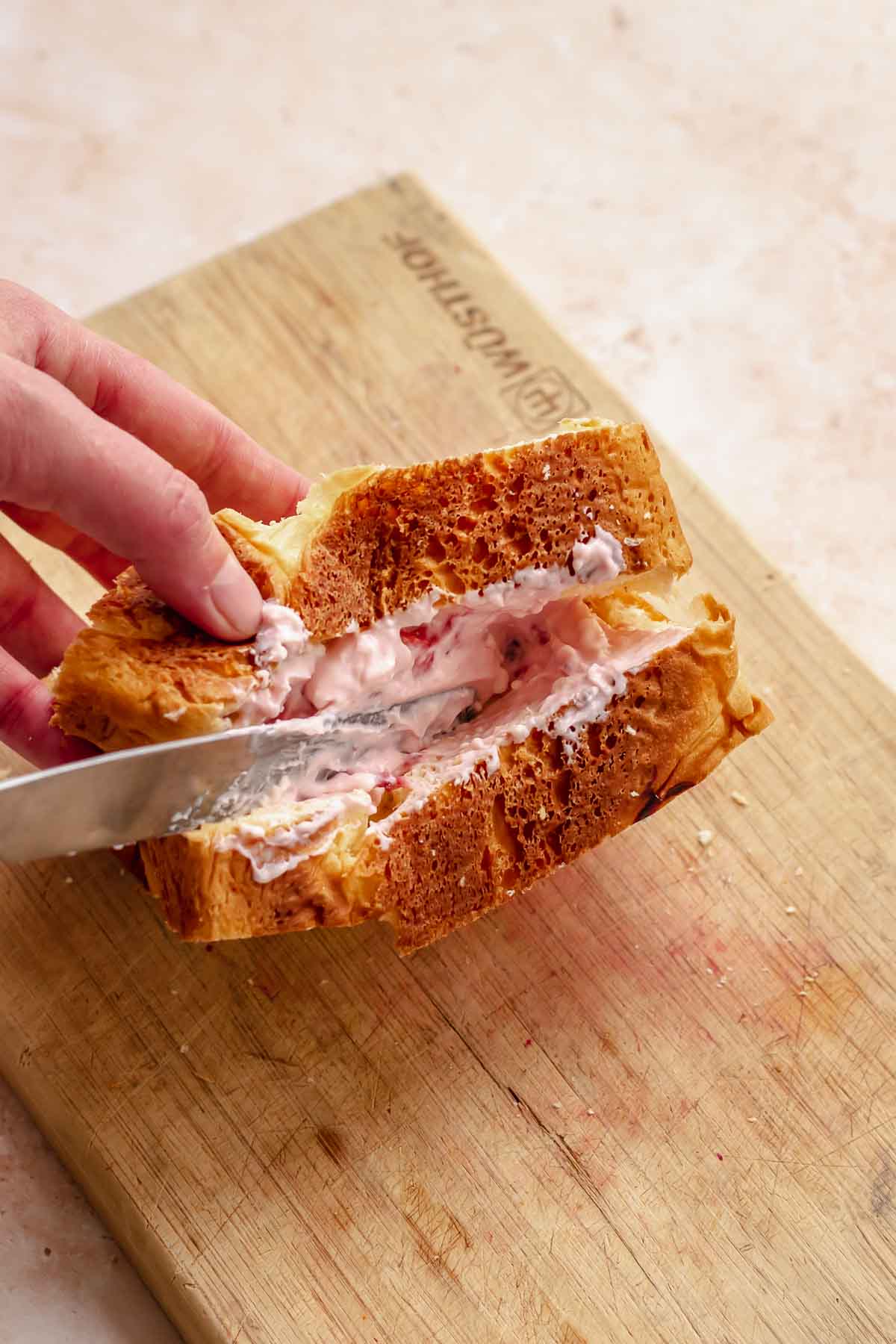 A hand uses a knife to add strawberry cream cheese into the brioche bread pocket.