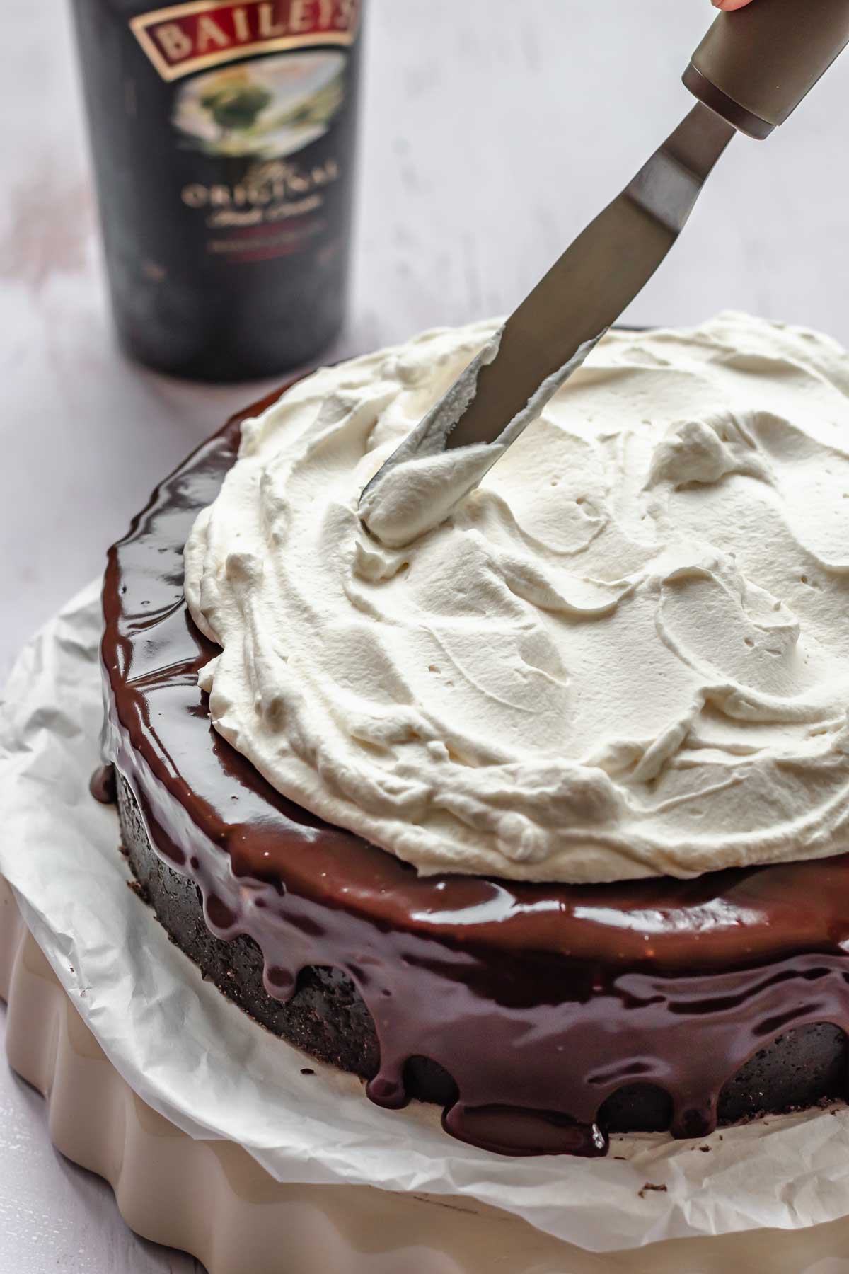 A spatula adds whipped cream on top of the ganache.