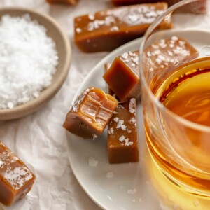 Salted caramels on a plate next to a glass of whiskey.
