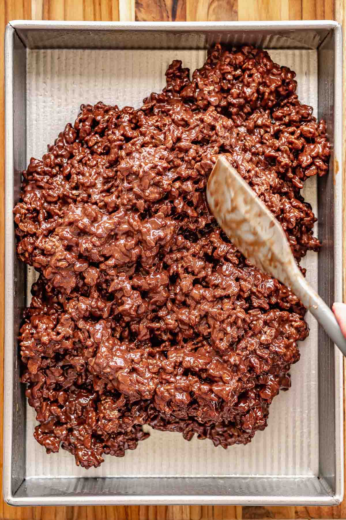 A spatula spreads chocolate Rice Krispies into a pan.