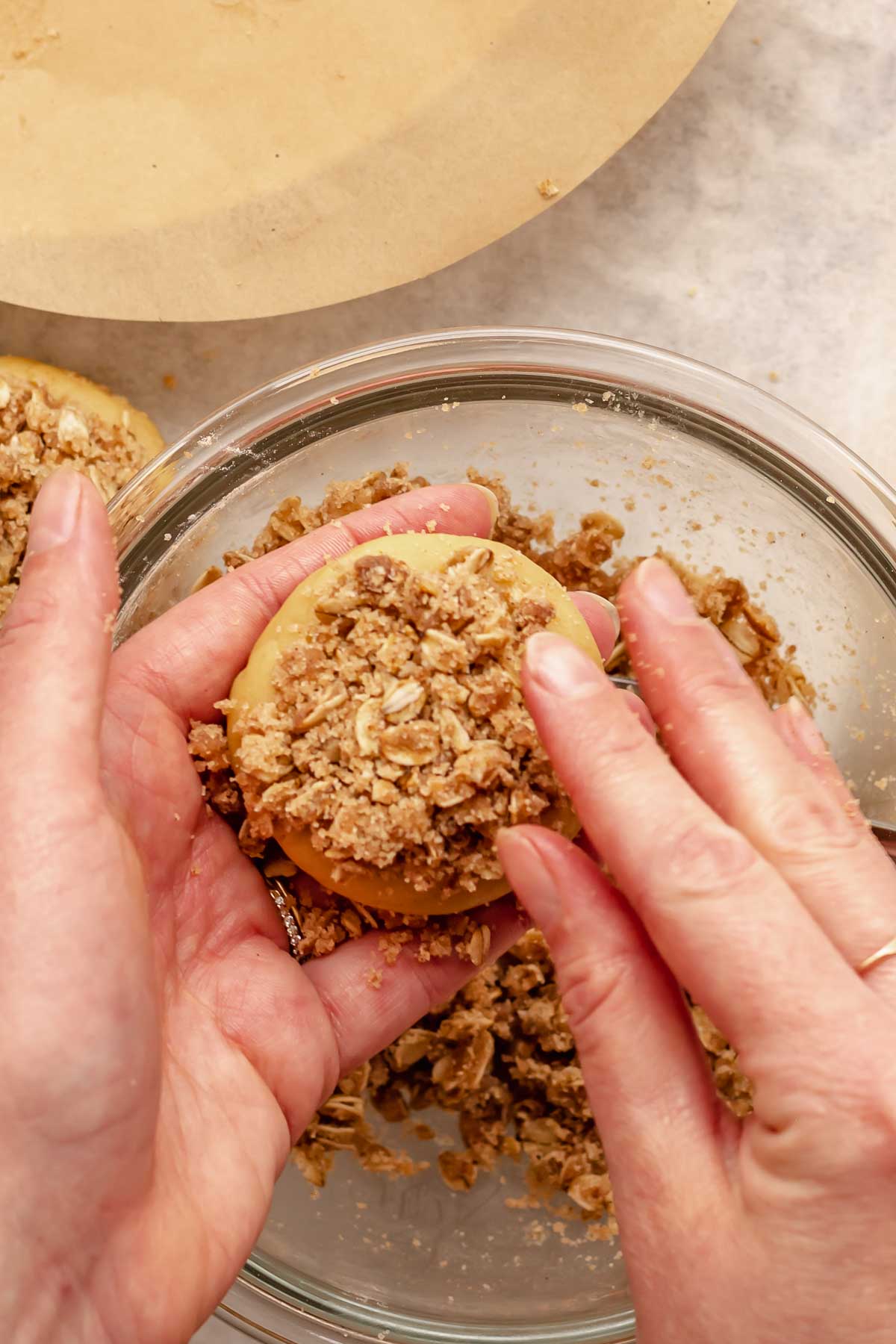 Hands push crumb topping onto the top of the cookie.