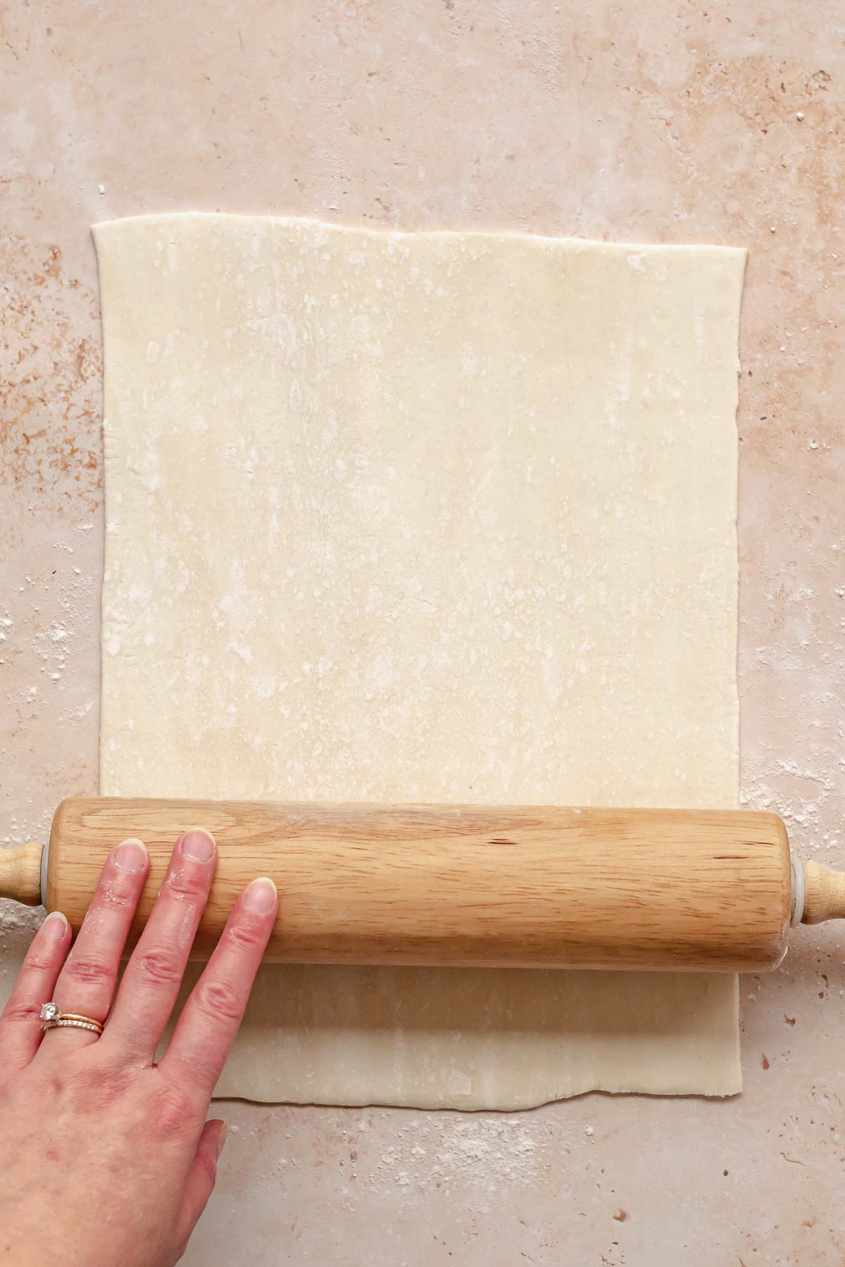 A rolling pin rolls out puff pastry into a rectangle.