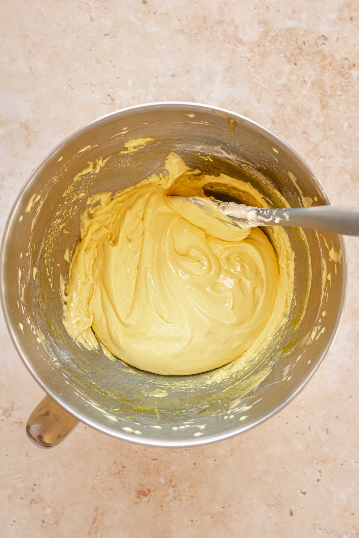 A spatula folds flour into egg yolk batter in a bowl.