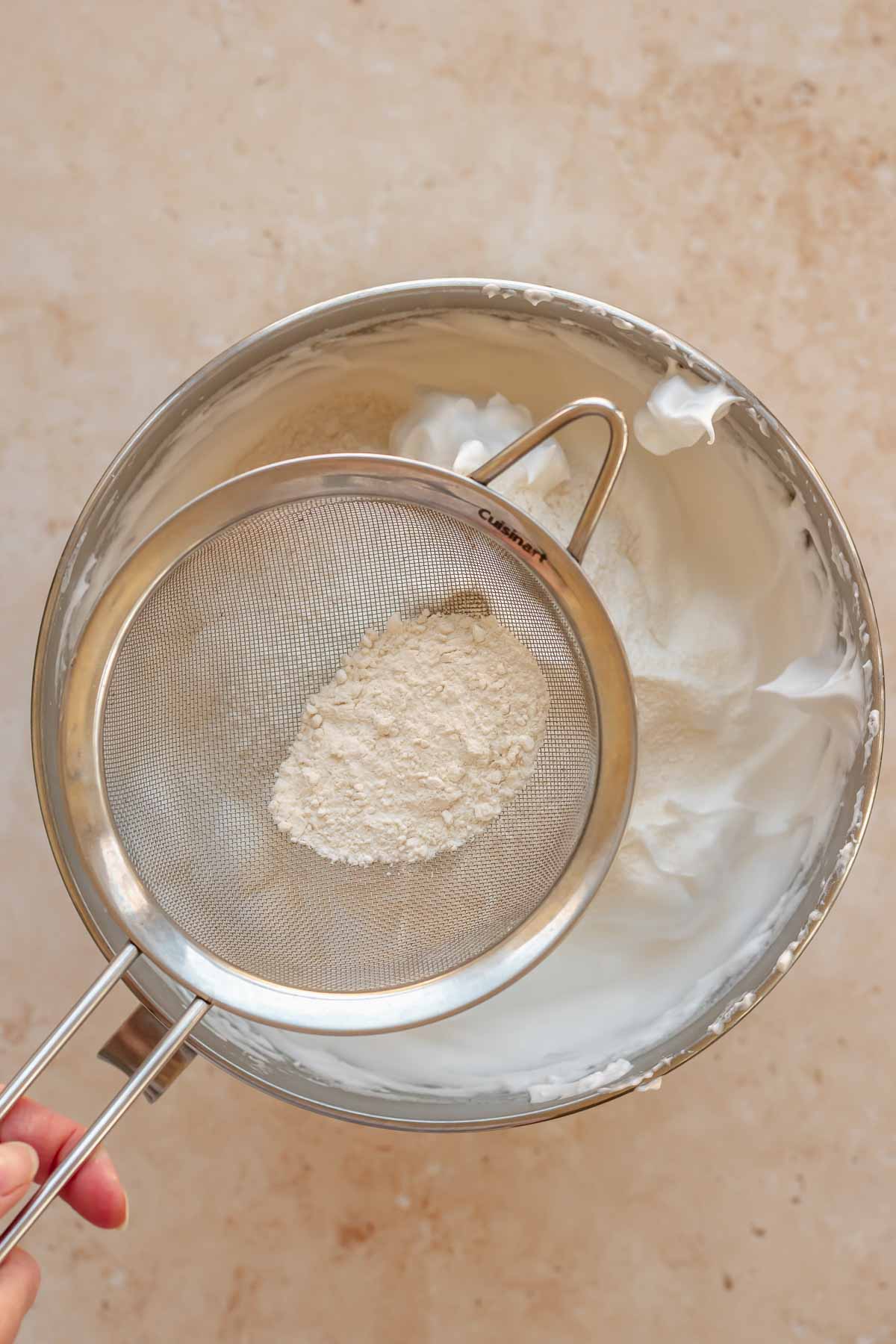 Flour in a sifter going into a bowl of whipped egg whites.