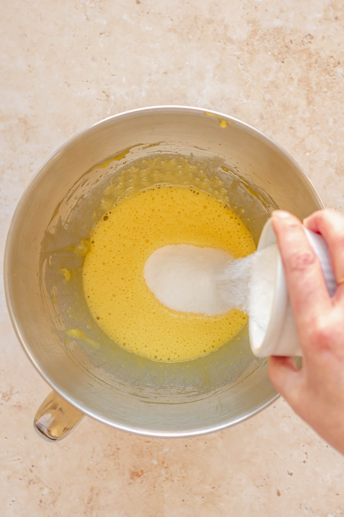 Sugar being poured into beaten egg yolks.
