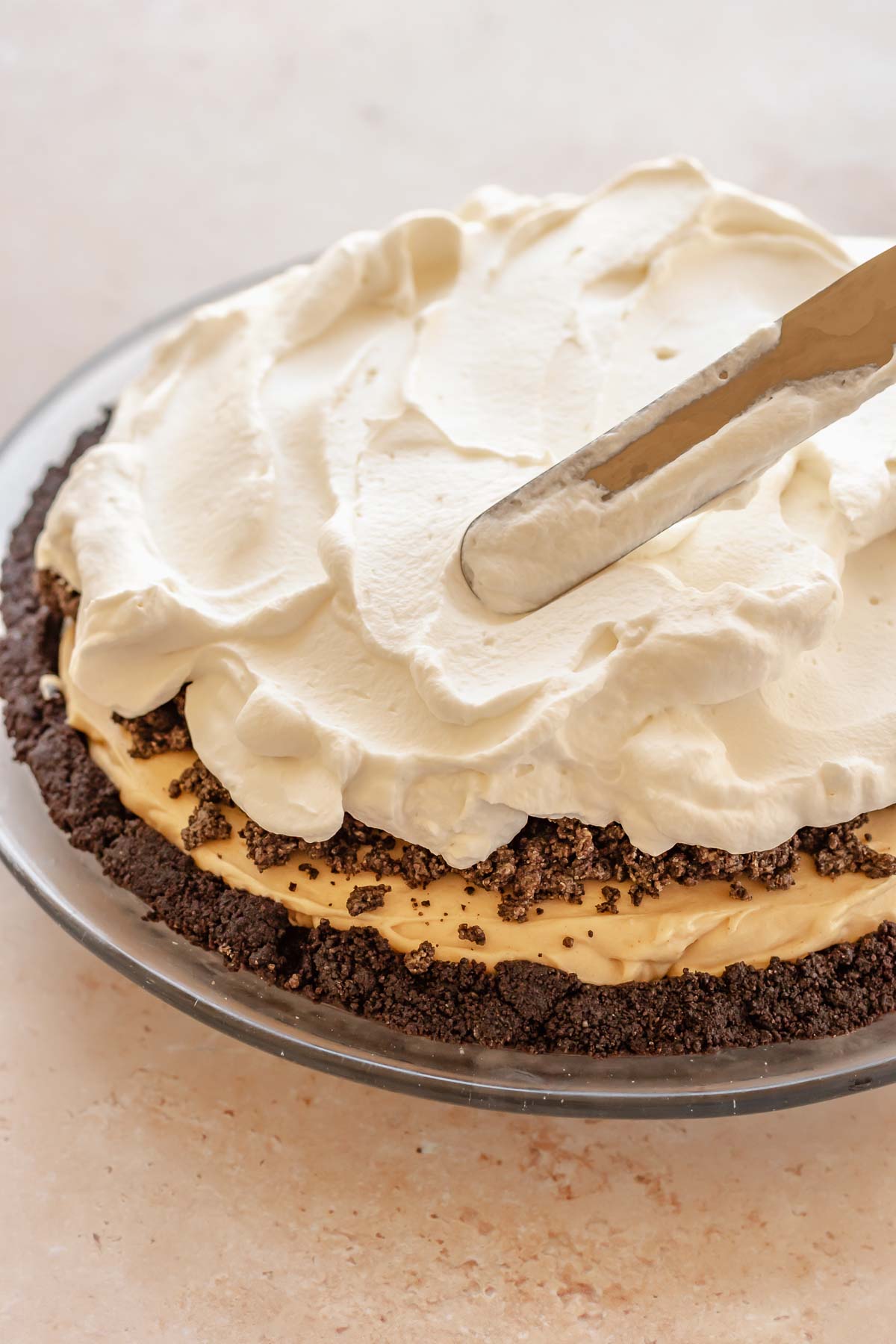 An offset spatula spreads whipped cream on top of the pie.
