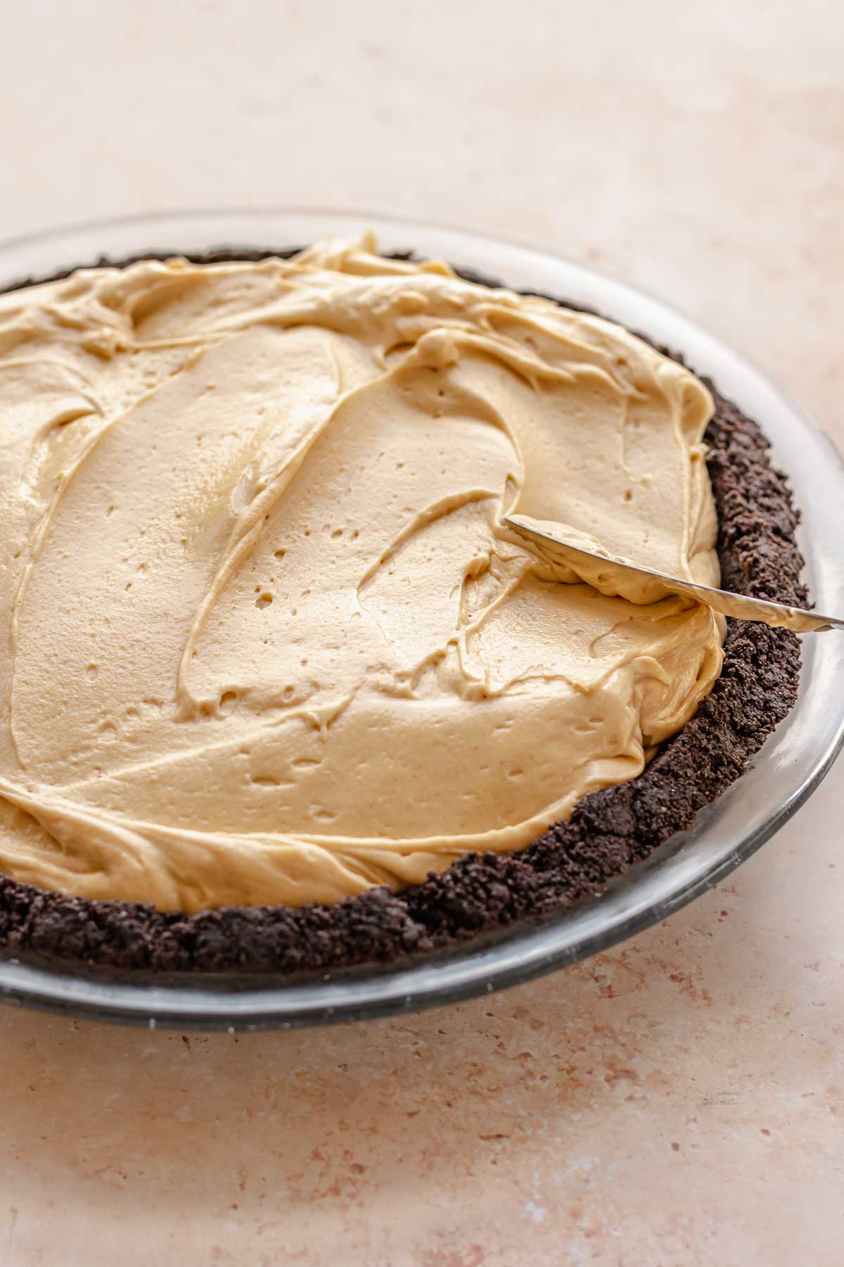 An offset spatula spreads peanut butter filling into oreo crust.