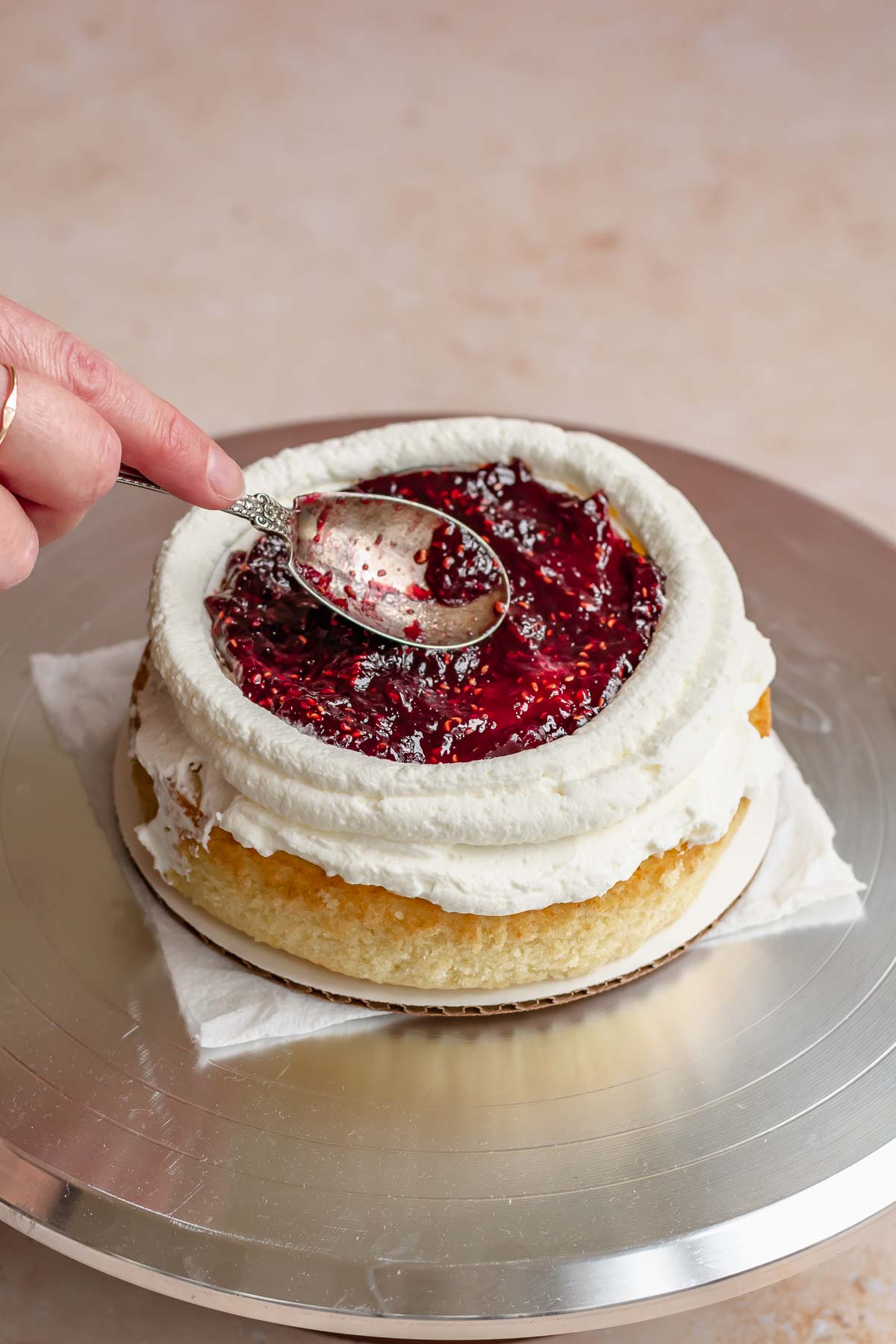 A spoon smooths raspberry jam into the center of the cake.