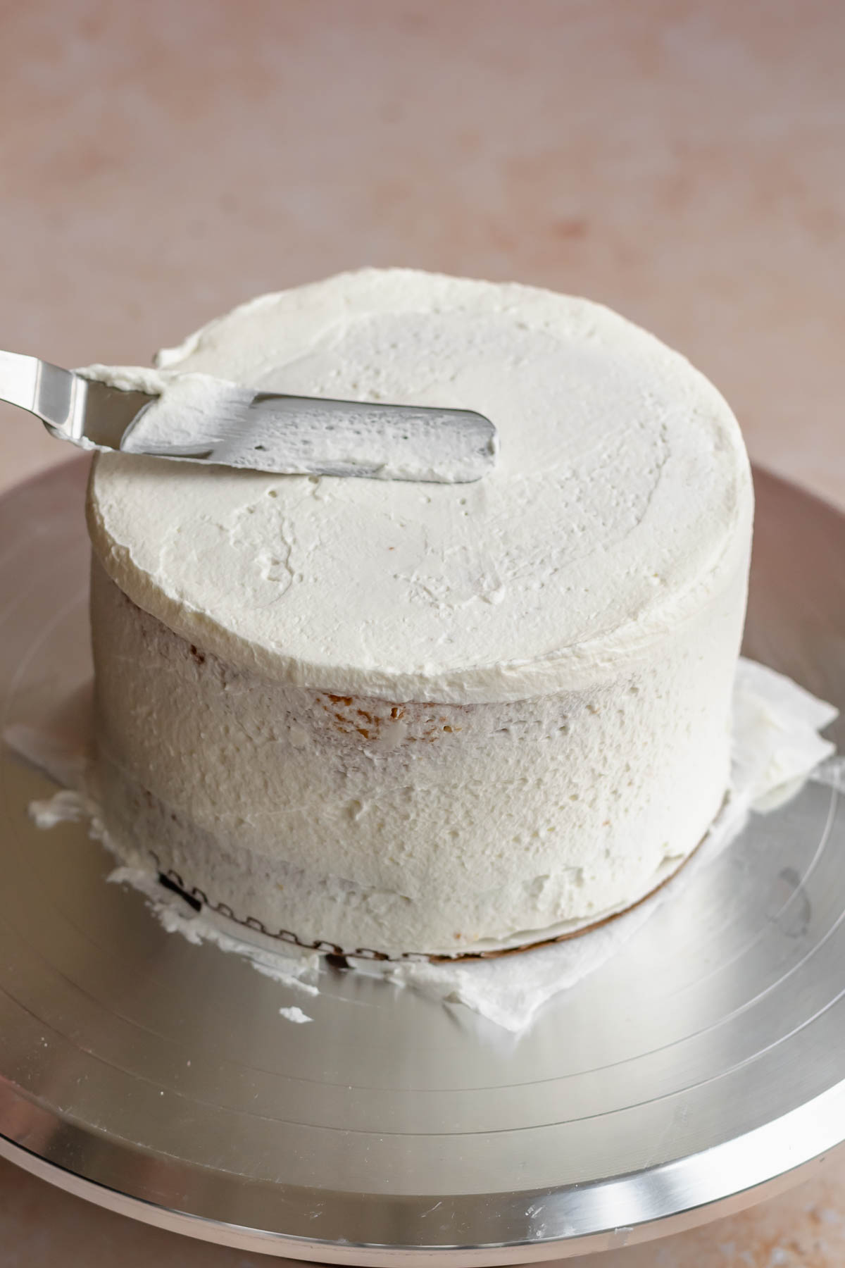 An offset spatula smooths frosting on top of the cake.