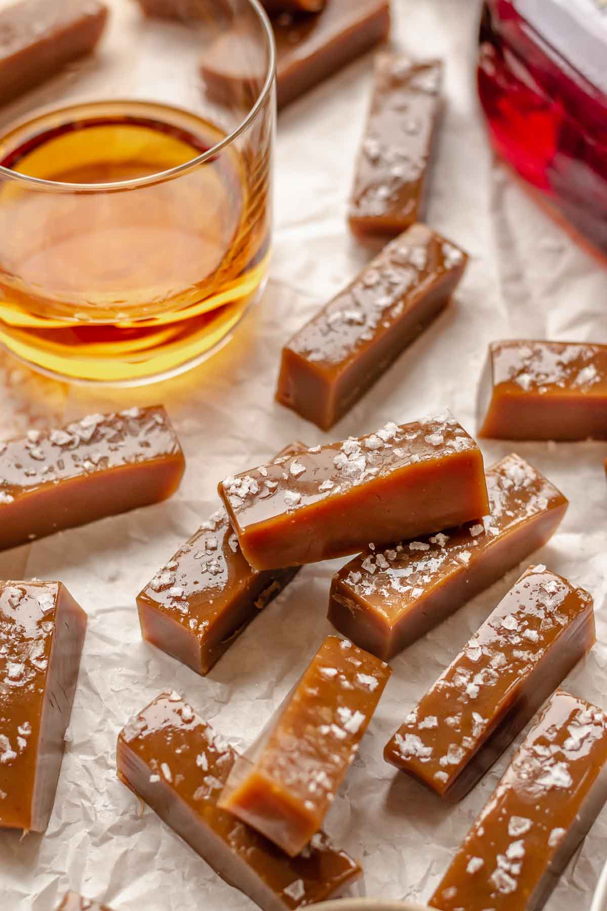 Salted whiskey caramels laid about with a glass of whiskey in the back.