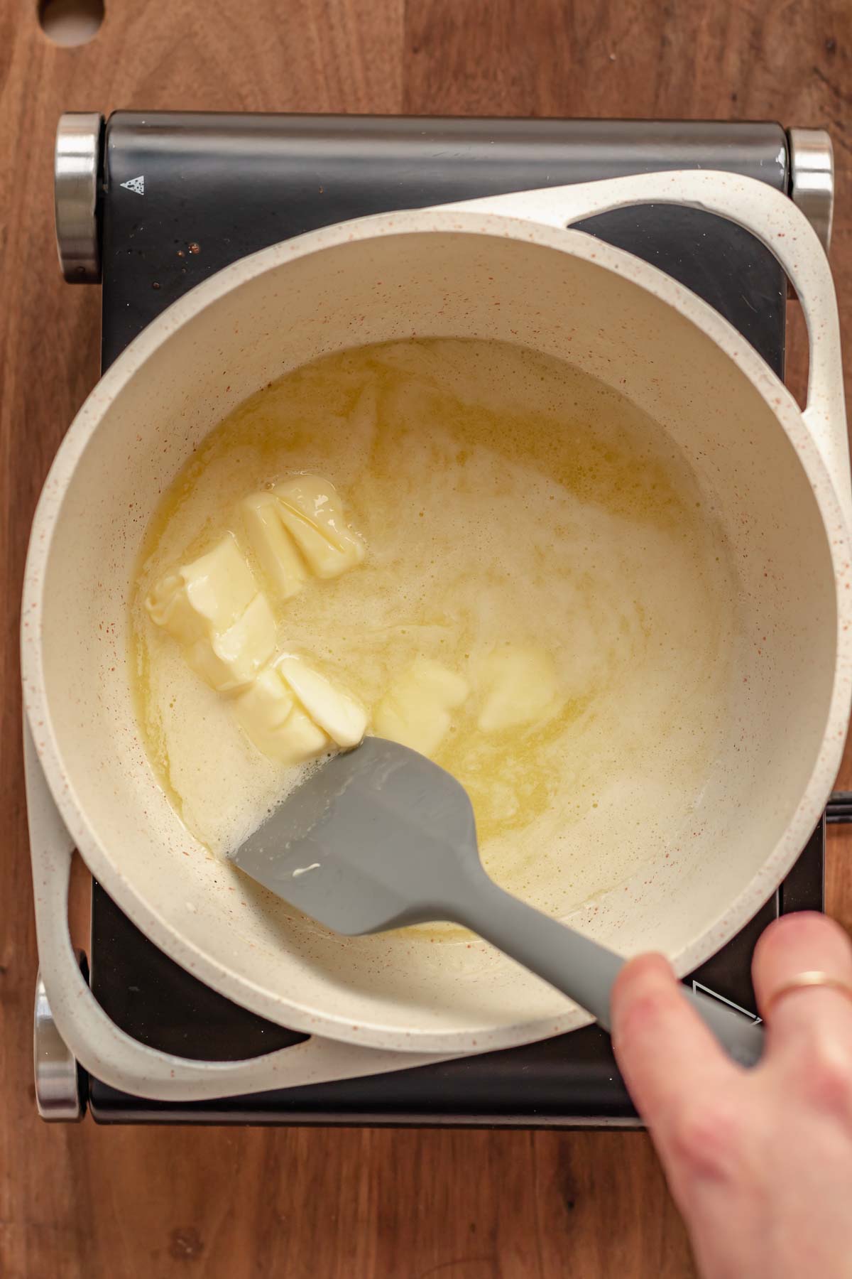 A spatula stirs melting butter in a pot.