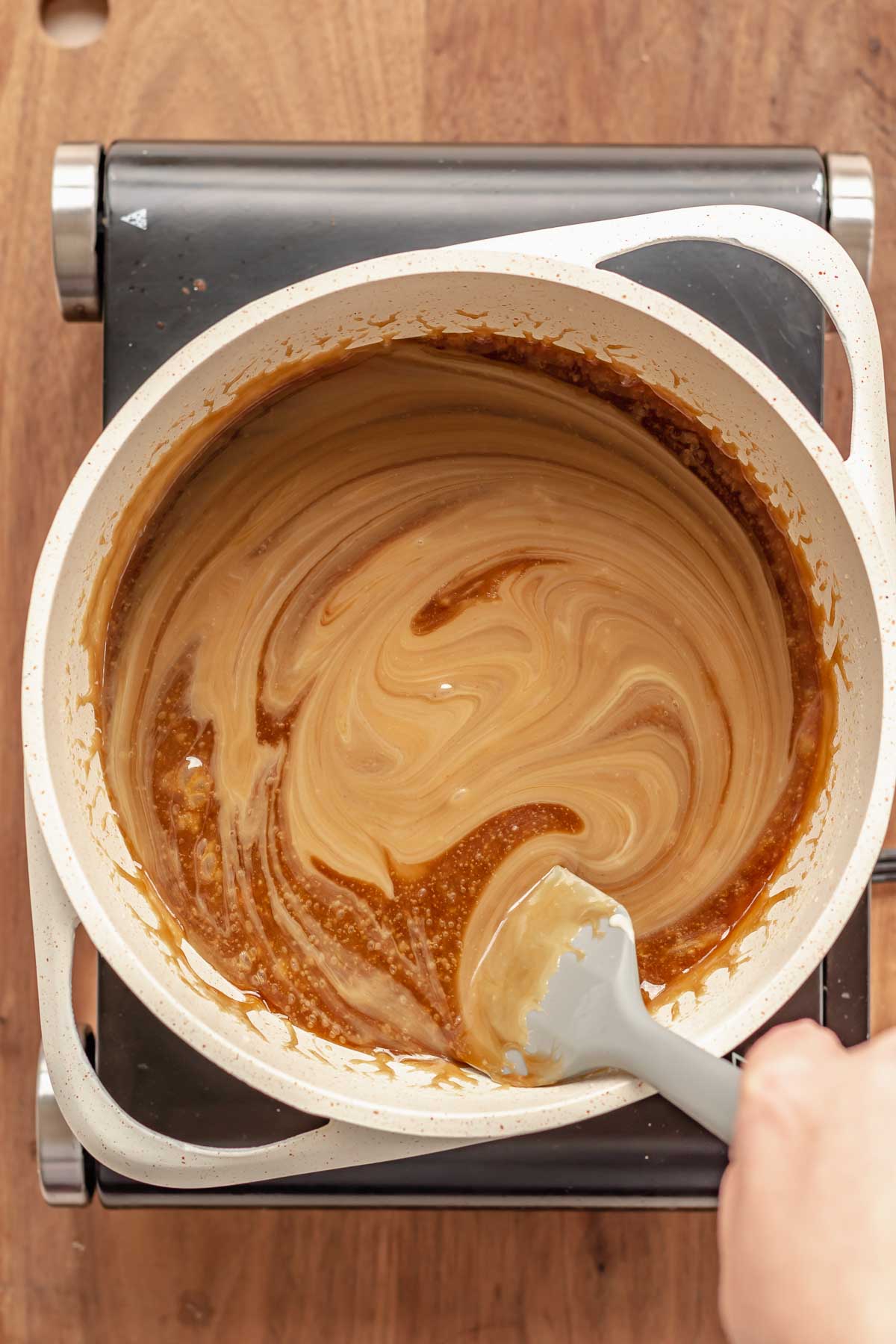 A spatula stirs sweetened condensed milk into a pot.