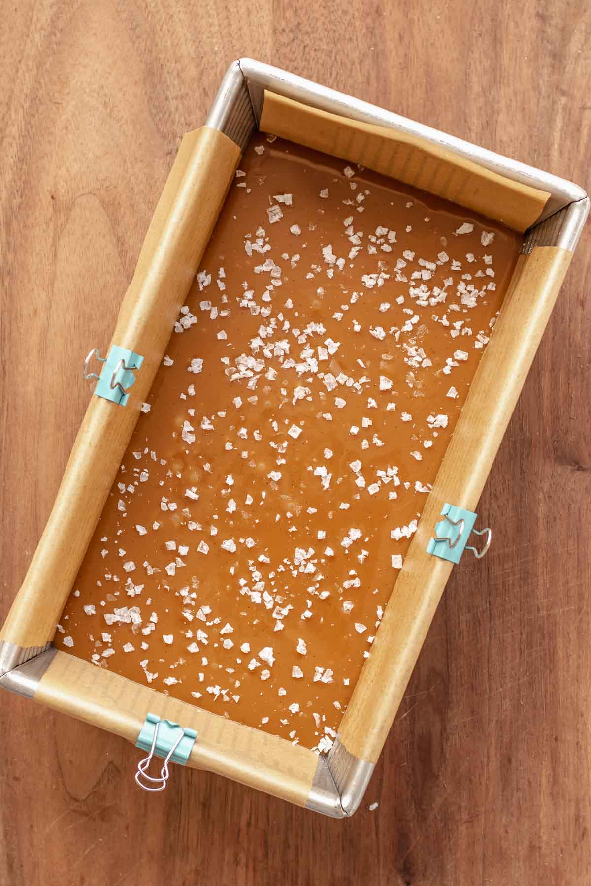 Flaky salt on top of set caramel in a loaf pan.