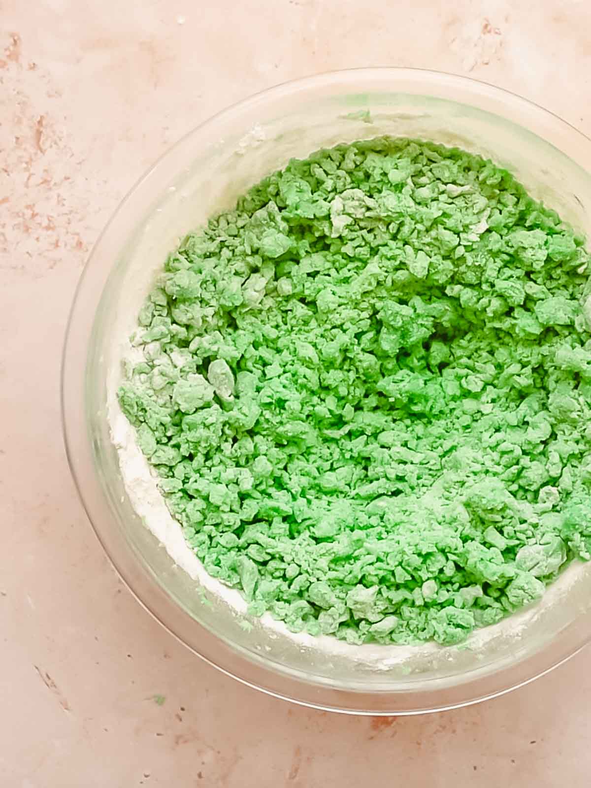 Green cookie dough in a bowl with flour being mixed in.