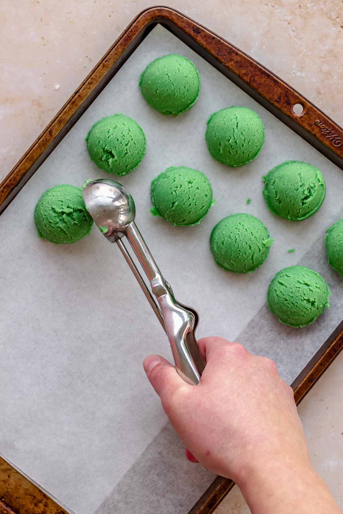A cookie scoop drops balls of cookie dough onto a cookie sheet.