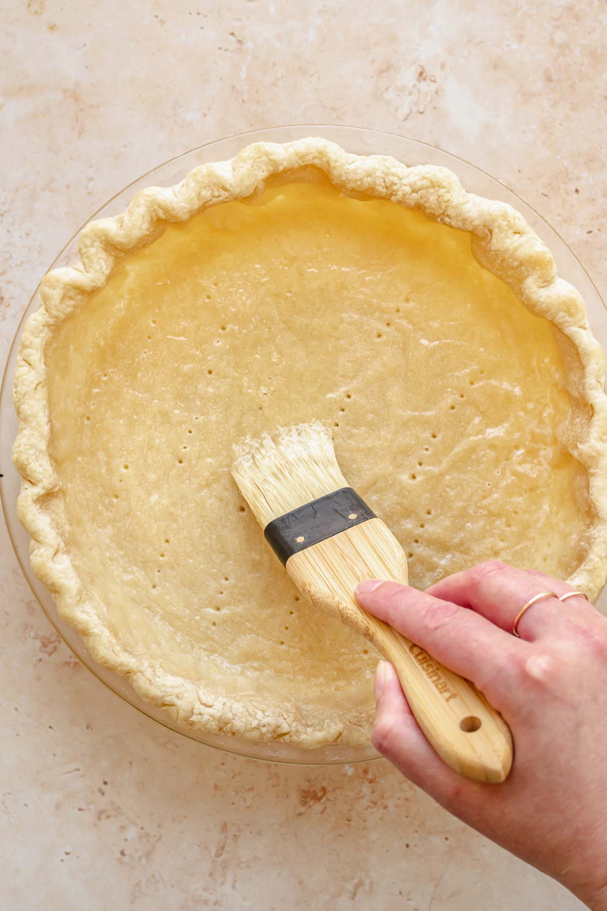 A pastry brush brushes egg whites into a par baked pie crust.
