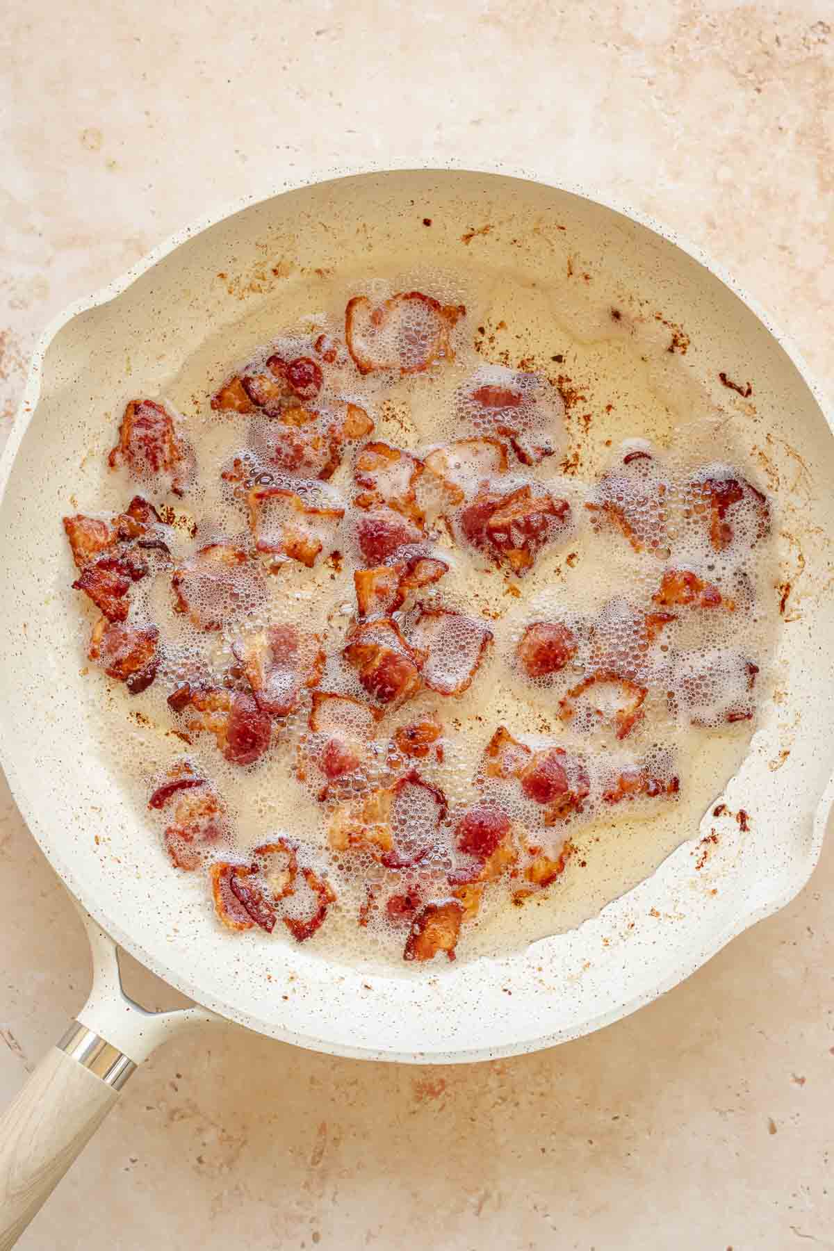 Bacon pieces cooking in a pan with grease.
