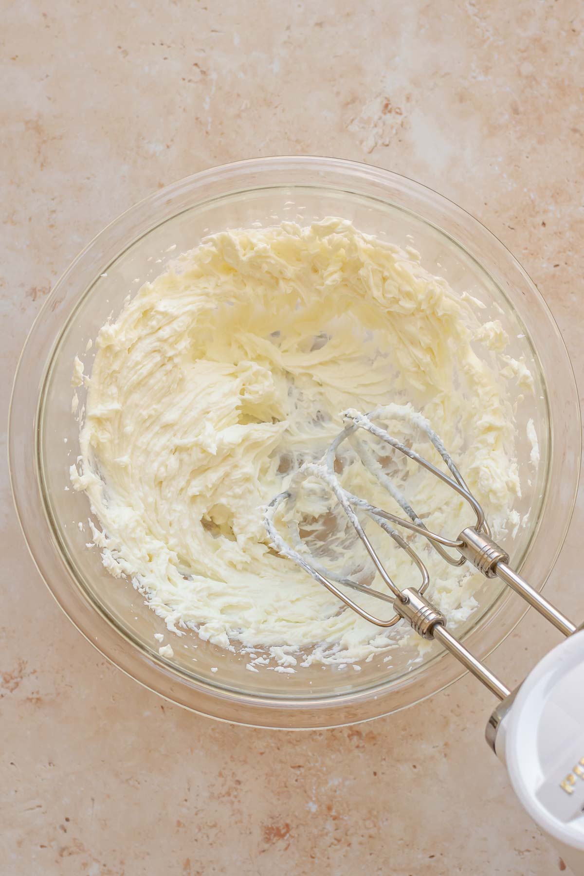 A hand mixer whips goat cheese in a bowl.