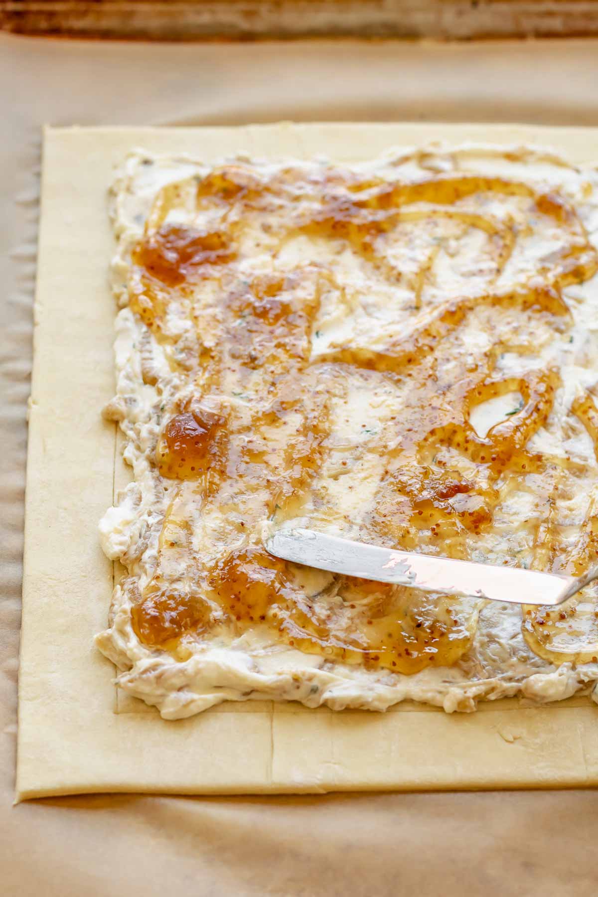 A spatula spreads fig jam on top of goat cheese and onions.