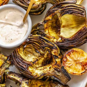 Grilled artichokes on a platter with dipping sauce.