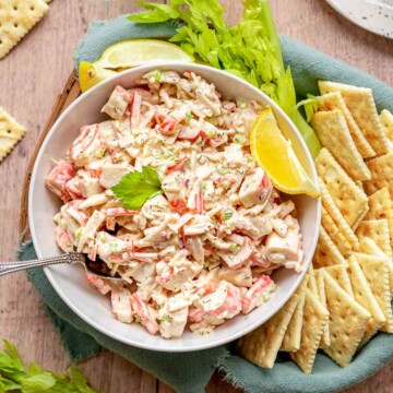 Imitation crab salad in a bowl with crackers, celery, and lemon.