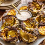 Marinated grilled artichokes on a platter with lemon aioli.