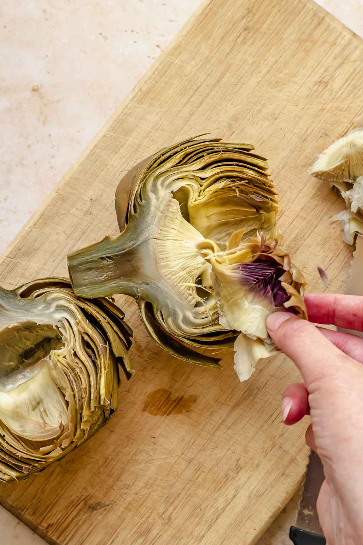 A hand removes the purple leaves from the inside of an artichoke.