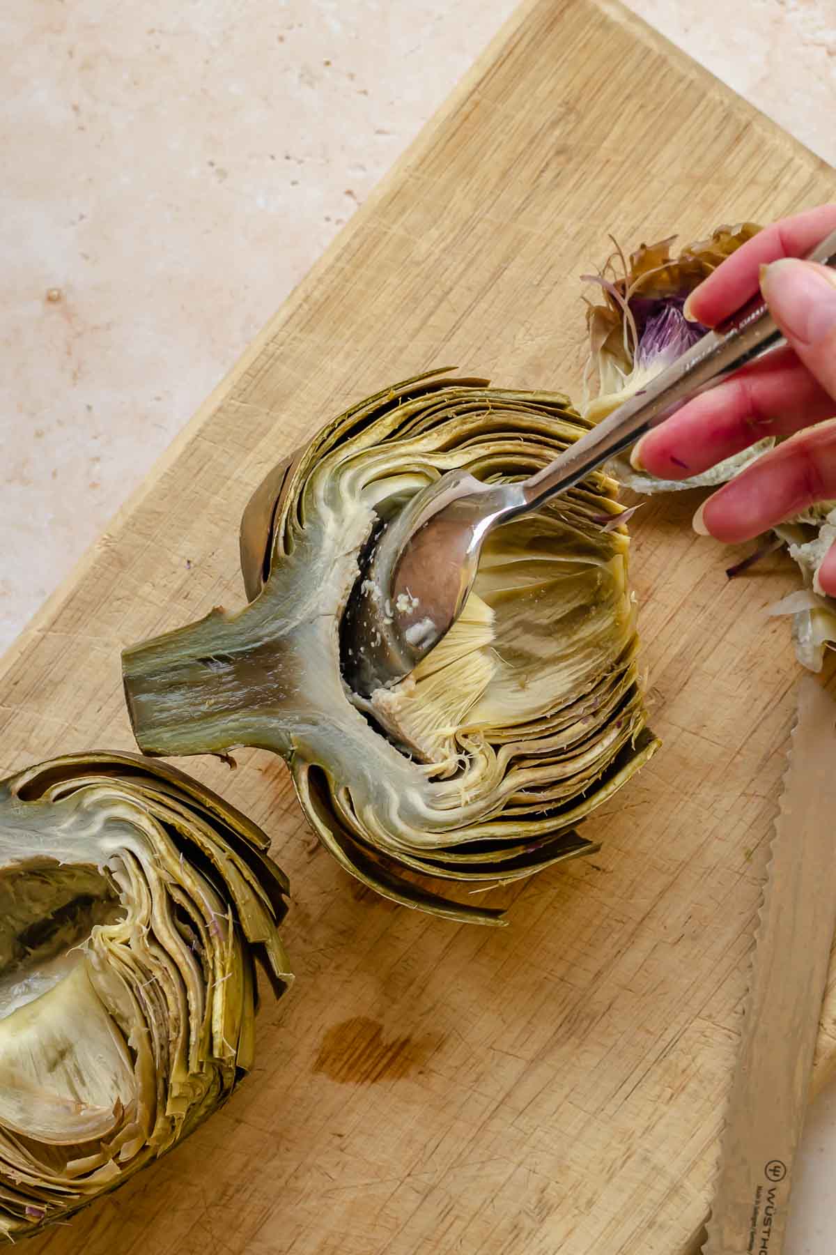 A spoon removes the choke from half of a steamed artichoke.