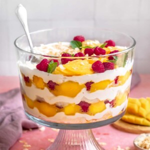 Mango trifle with a spoon it is showing the layers on the sides.