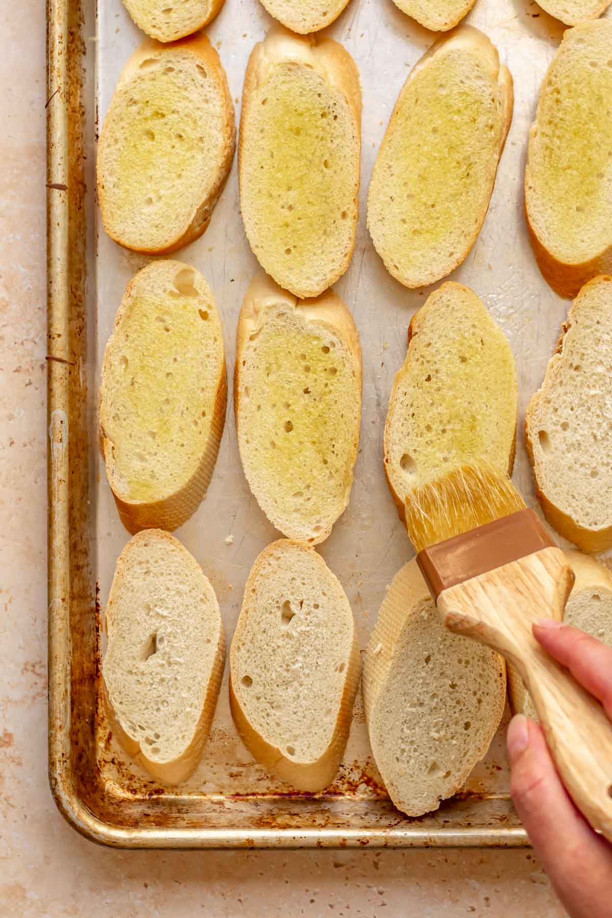 A brush adds olive oil onto bread slices.