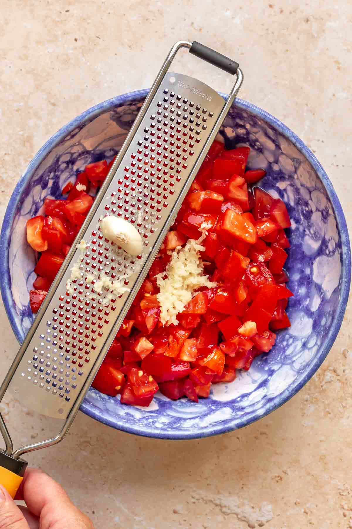A garlic clove being grated into tomatoes.