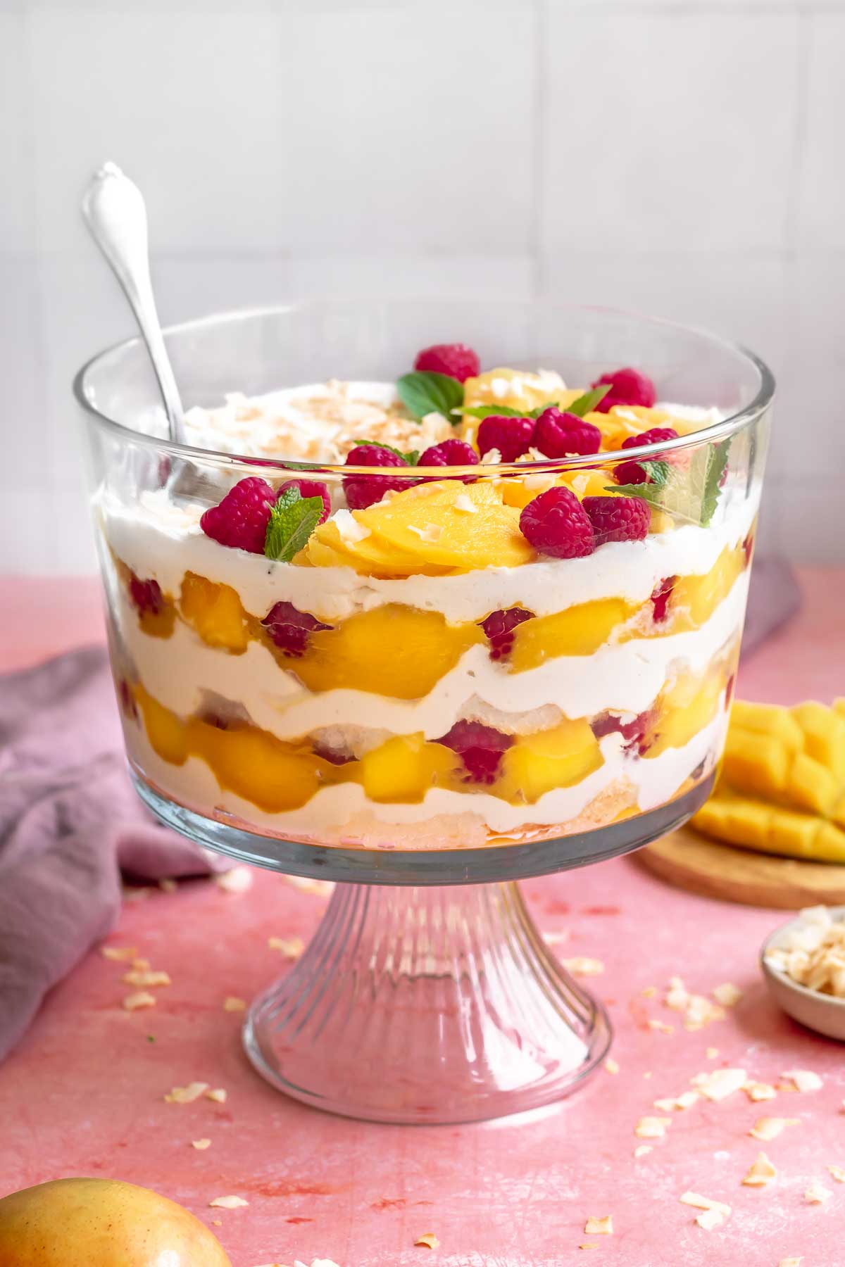 Mango trifle with a spoon it is showing the layers on the sides.