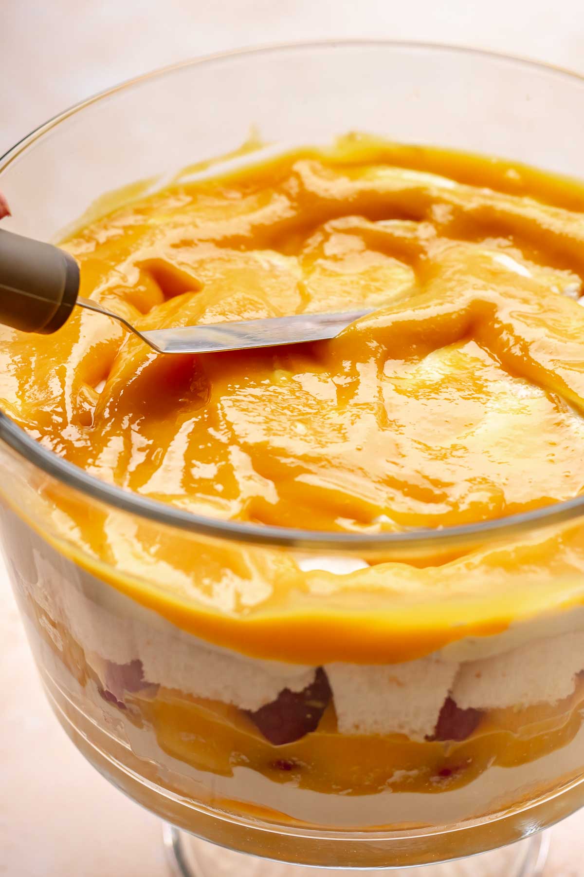 Mango puree being spread onto the trifle ingredients.