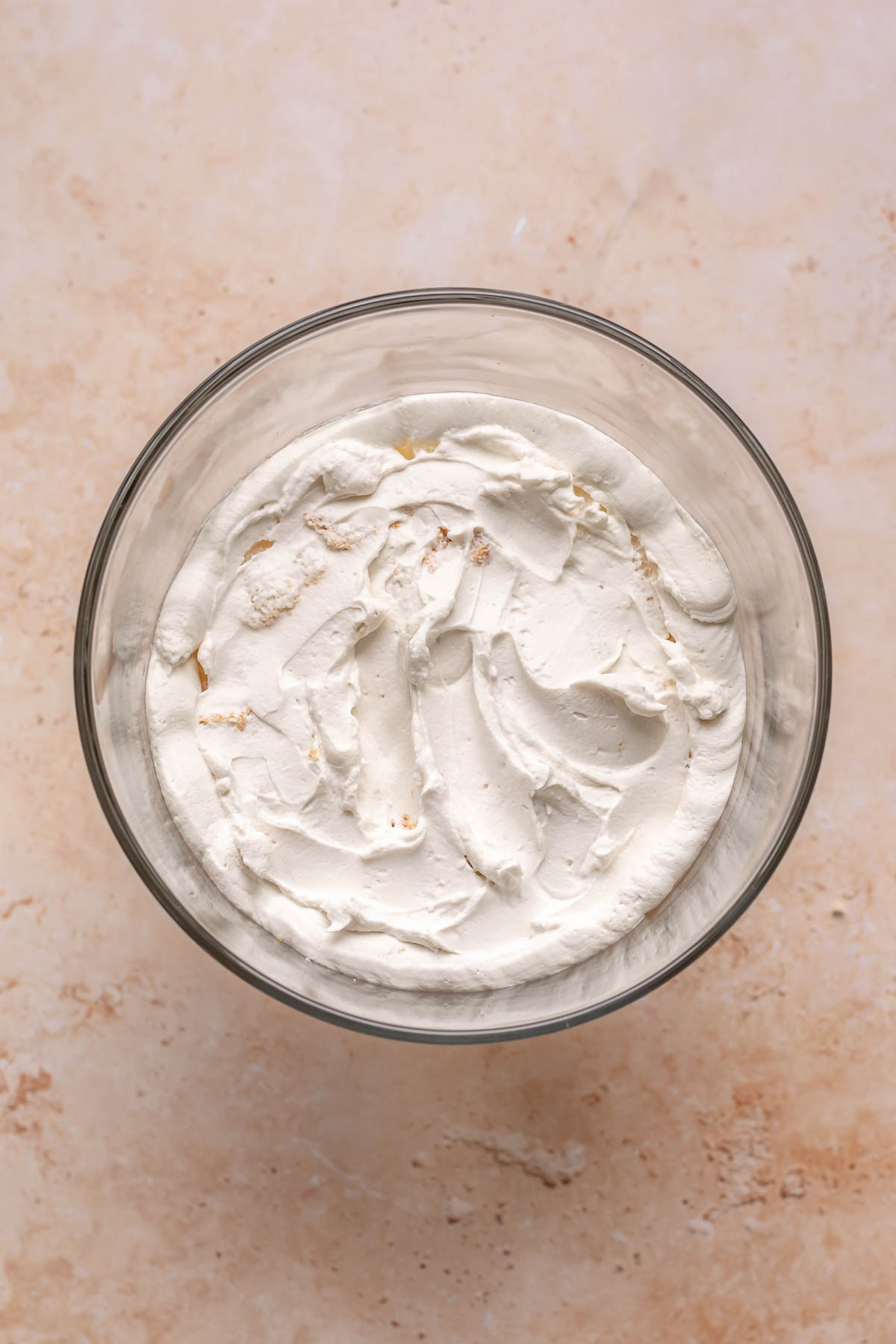 Coconut whipped cream spread on top of angel food cake layer in a bowl.