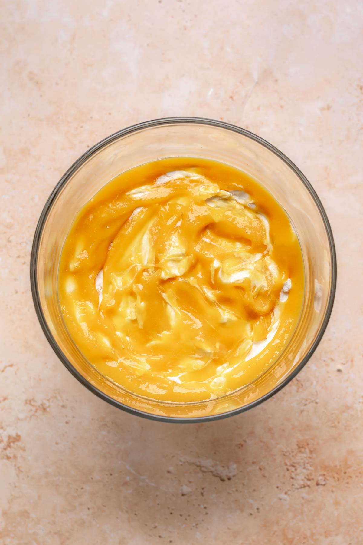 Mango puree spread on top of coconut whipped cream in a bowl.