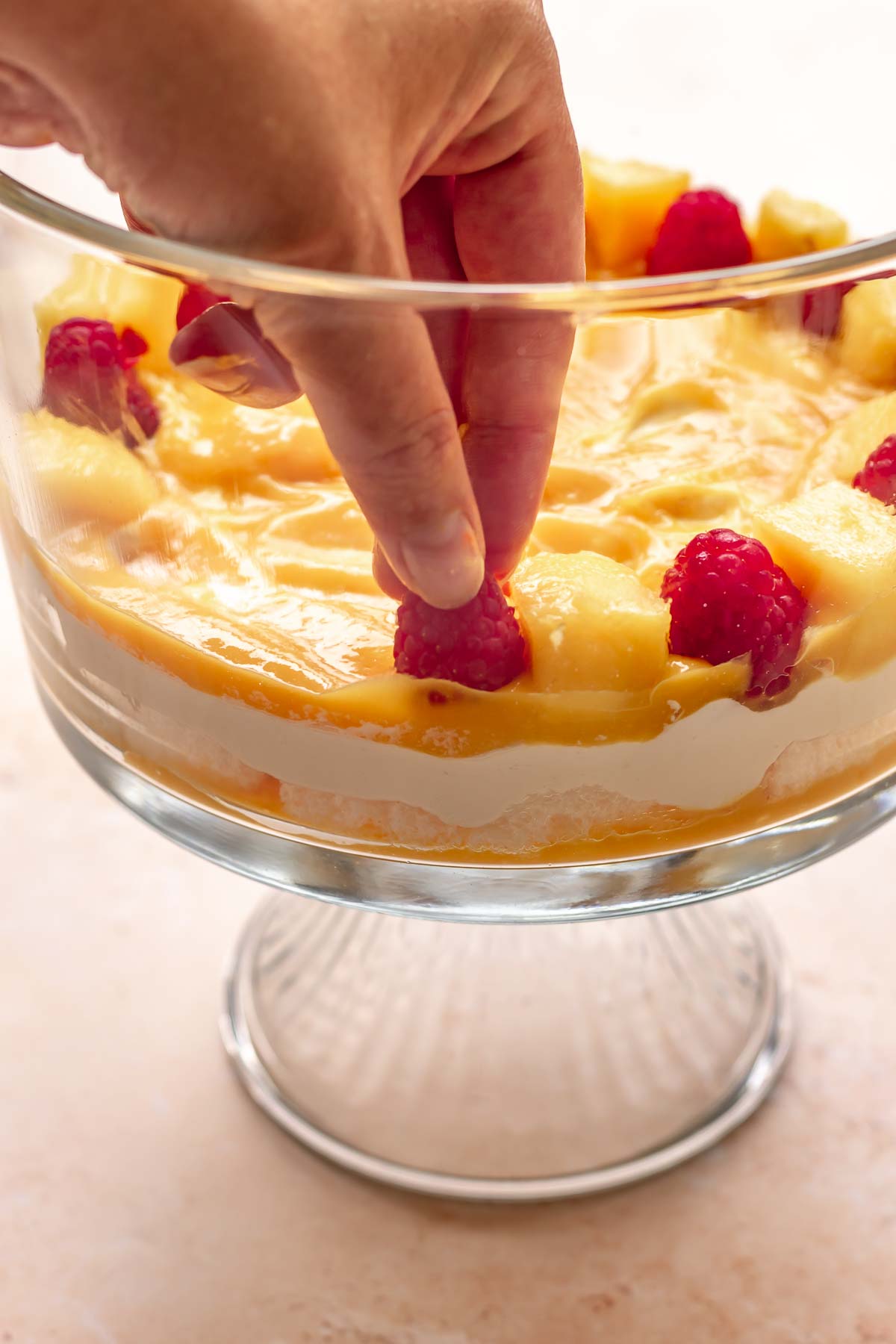 A hands adds a raspberry next to a piece of mango on the edge of the bowl.