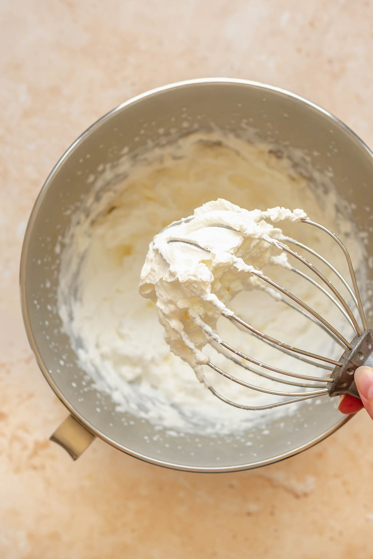 Stiff peaks of whipped cream on the tip of a whisk.