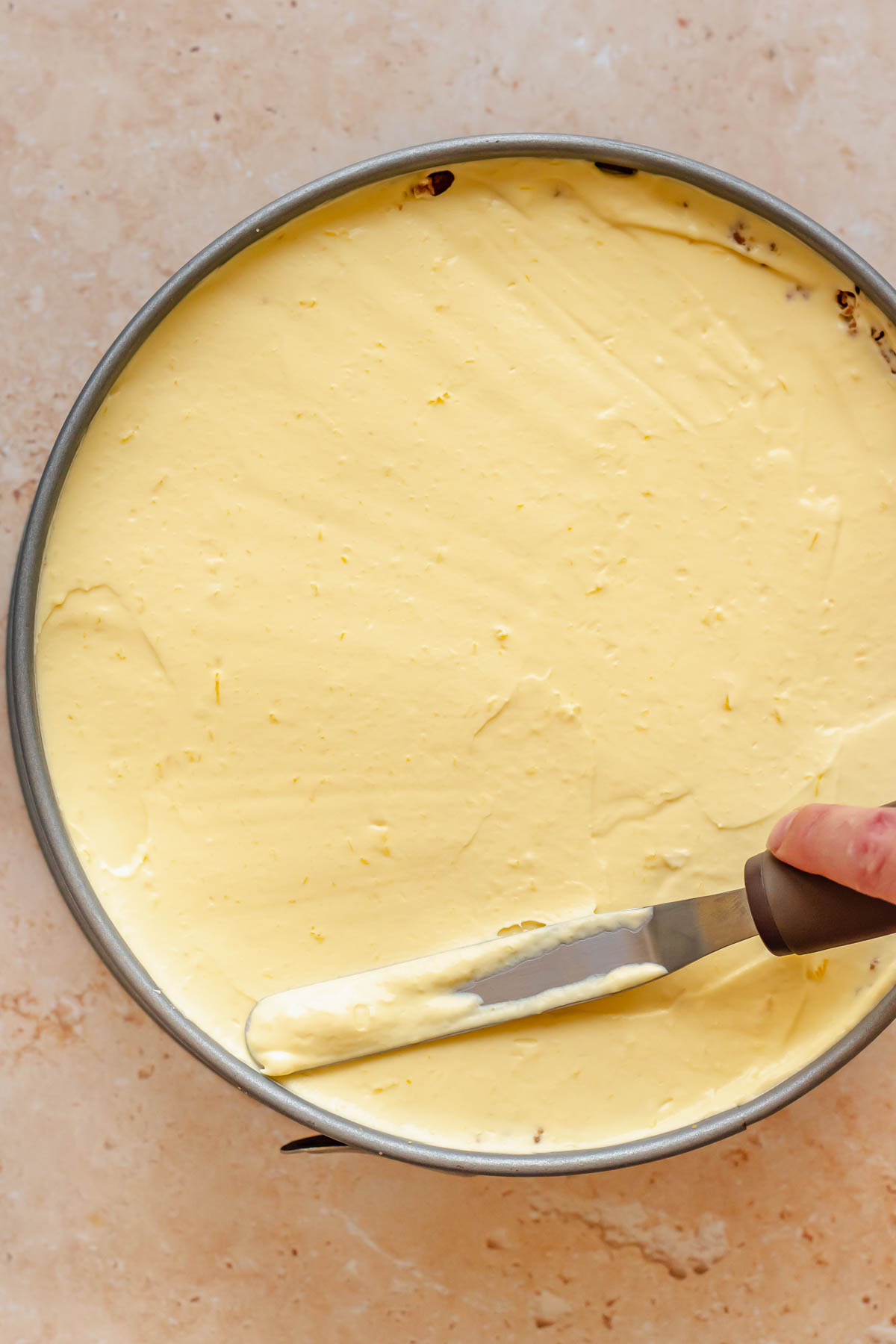 A spatula smooths mango cheesecake batter into a springform pan.