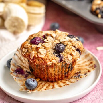 Banana blueberry oat muffin on a plate with the cupcake liner removed.