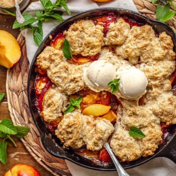 Skillet peach cobbler with a serving spoon in it.