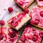 Slices of white chocolate raspberry cheesecake bars on a wire rack.