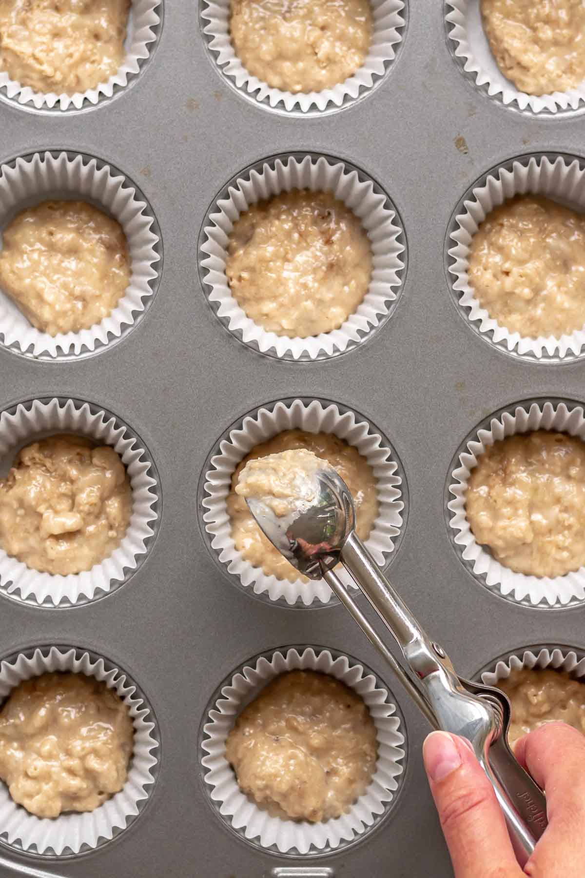 A cookie scoop adds a small amount of muffin batter to cupcake liners.
