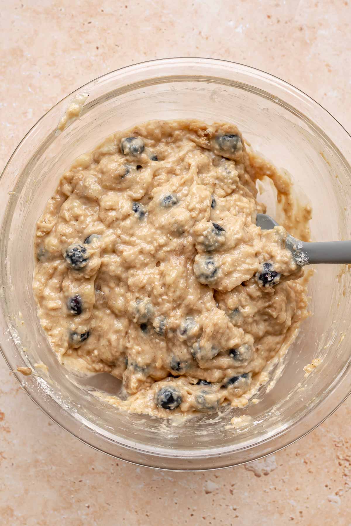 A spatula folds blueberries into muffin batter.
