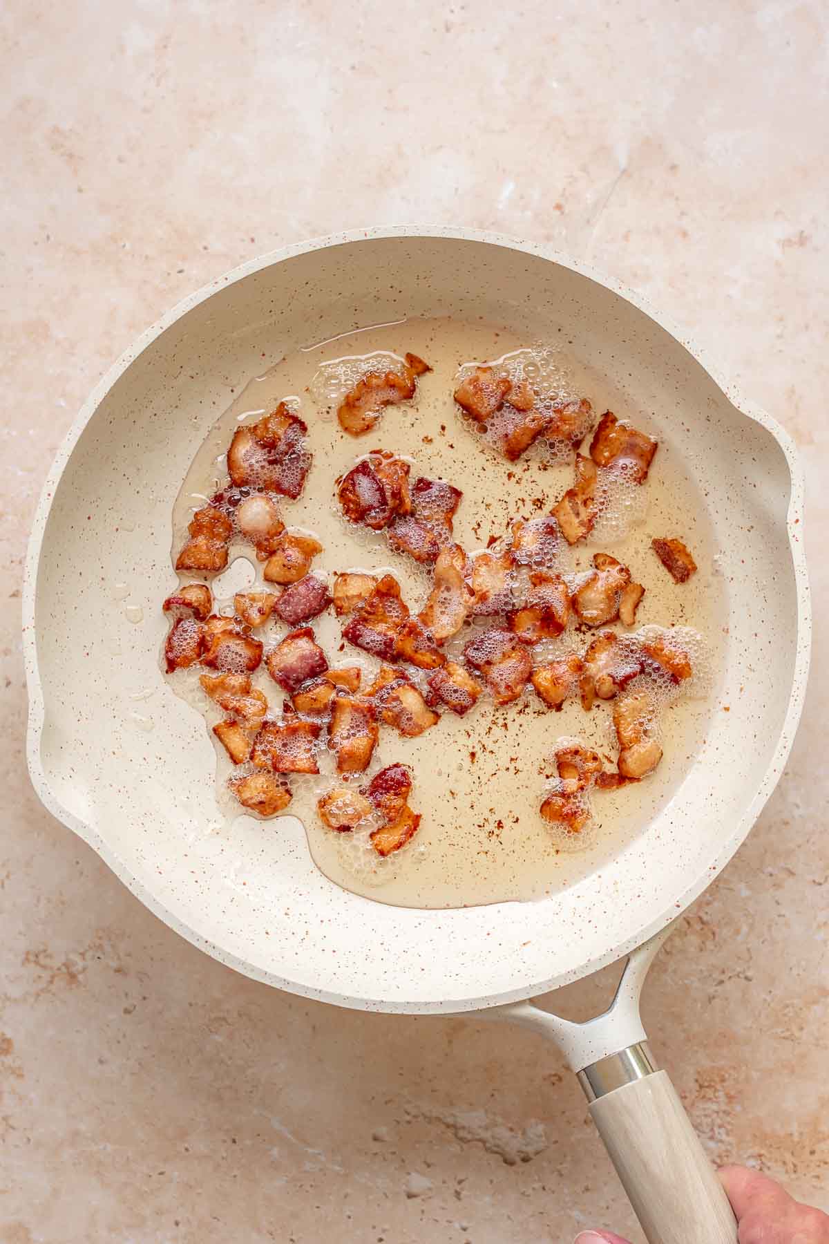 Bacon pieces frying in a pan.