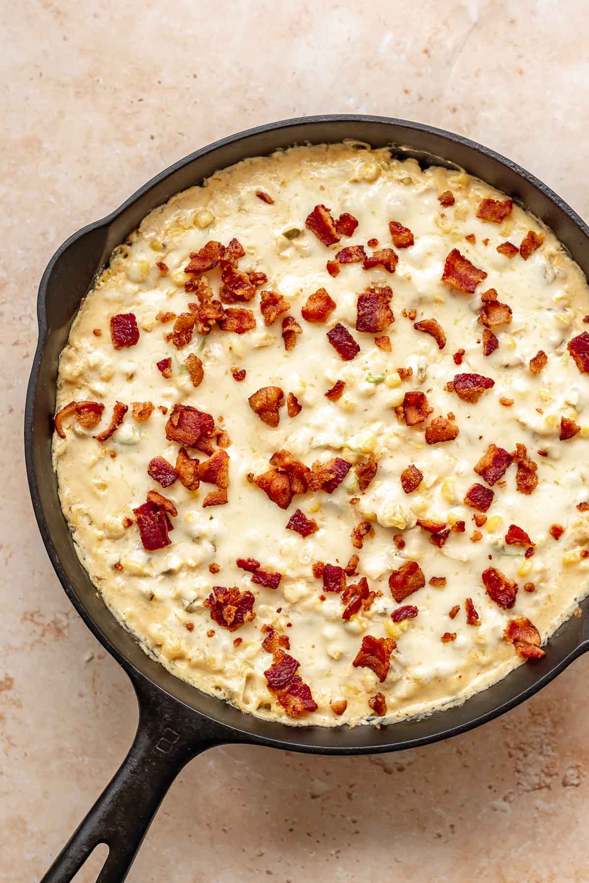Hot corn dip in a skillet with melted cheese and cooked bacon pieces on the top.
