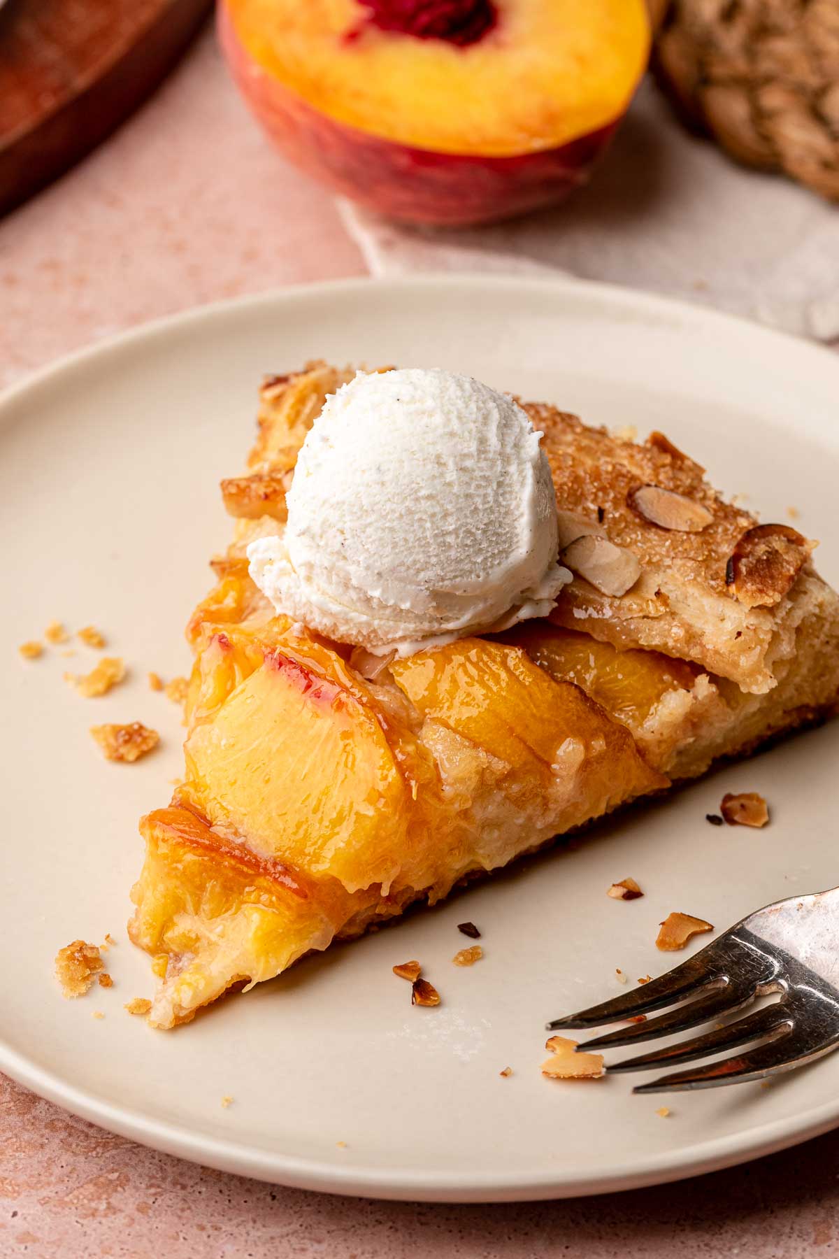 A slice of peach galette on a plate with a scoop of ice cream on top.