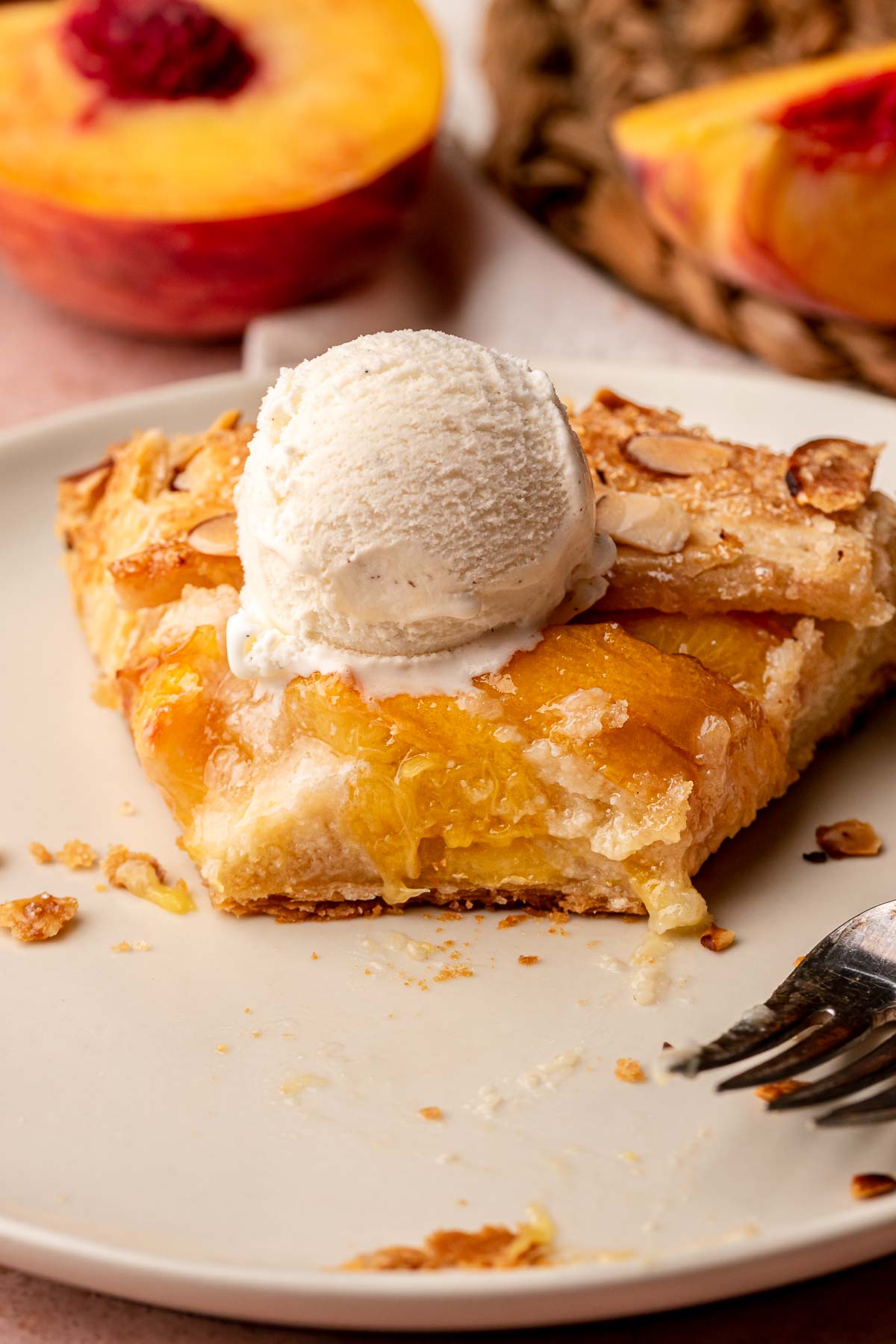 A slice of peach galette on a plate with a scoop of ice cream on top.