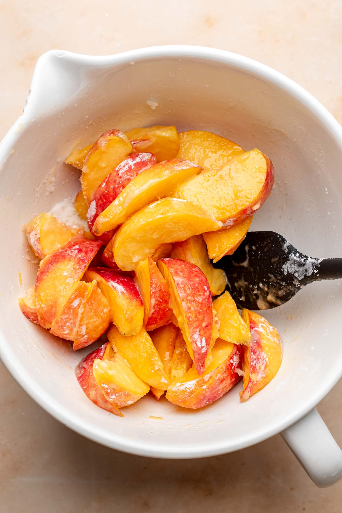 A rubber spatula tosses peaches in a bowl.