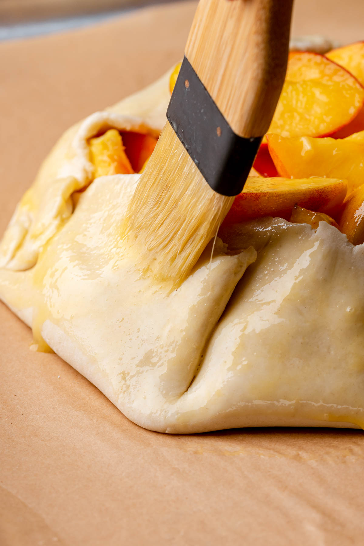 A pastry brush swipes egg wash onto the crust.