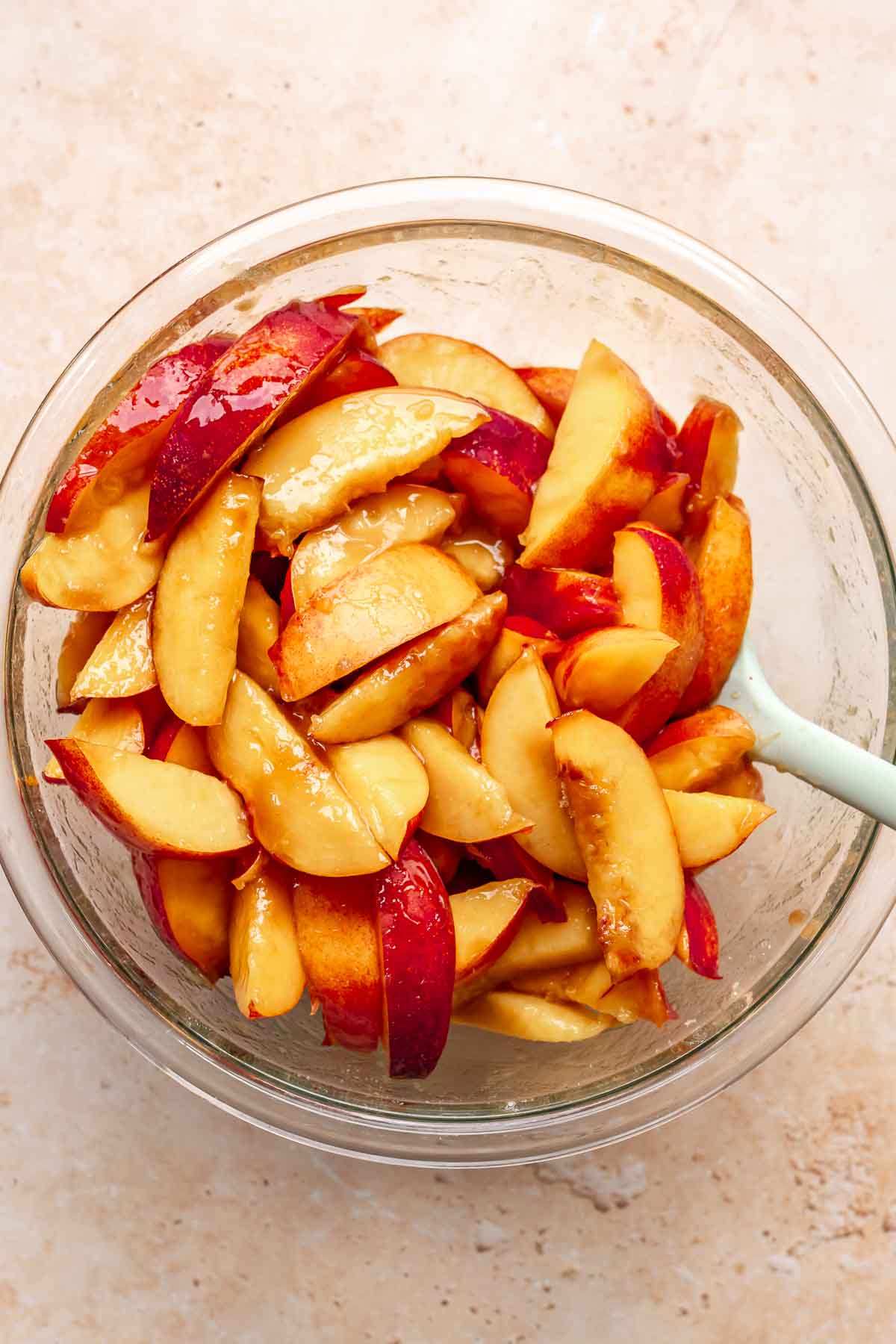 Sliced peaches in a bowl with a spatula.